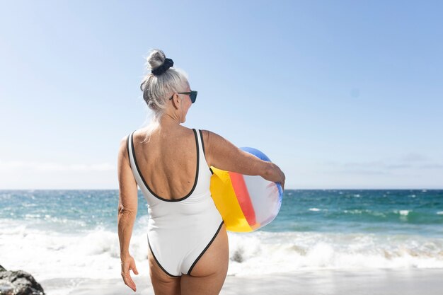 Dojrzała kobieta trzyma piłkę plażową w stroju kąpielowym