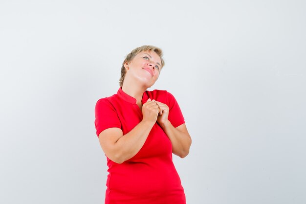 Dojrzała kobieta trzymając się za ręce na klatce piersiowej w czerwonej koszulce i rozmarzona.