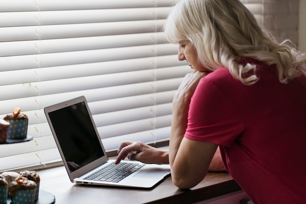 Dojrzała kobieta używa laptop blisko okno