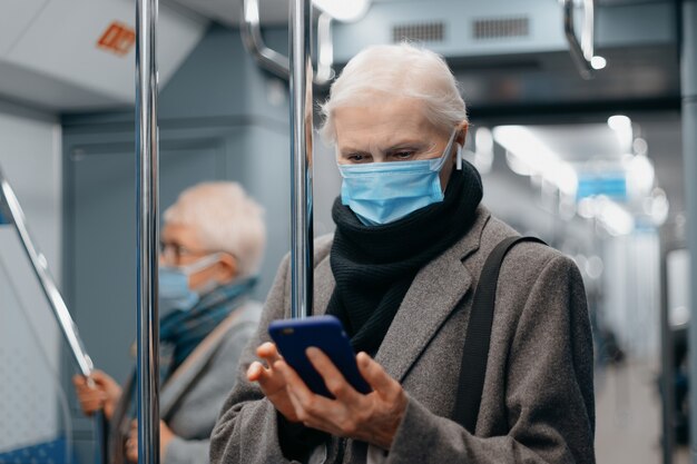 Dojrzała kobieta w masce ochronnej czyta wiadomość stojącą w wagonie metra