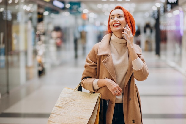 Dojrzała kobieta z torbami na zakupy w centrum handlowym przy użyciu telefonu