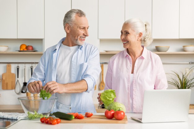 Dojrzała kochająca pary rodzina używa laptop i kulinarną sałatki