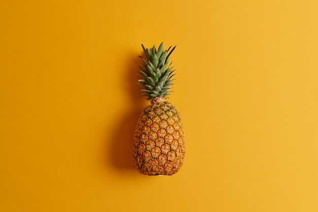 Dojrzały ananas na białym tle na żółtym tle. Egzotyczne owoce o niskiej zawartości kalorii, pełne składników odżywczych i przeciwutleniaczy, można spożywać na wiele sposobów lub dodawać do diety. Składnik do sporządzania soku