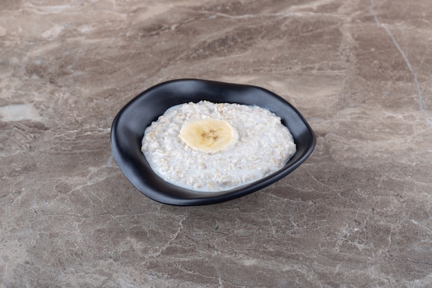 Bezpłatne zdjęcie dojrzały banan pokrojony w plasterki na misce owsianki, na marmurowej powierzchni