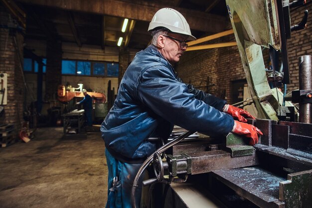 Dojrzały, doświadczony pracownik tnie metal za pomocą specjalnej obrabiarki.