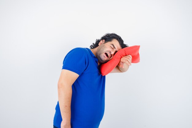 Dojrzały mężczyzna w niebieskiej koszulce, opierając głowę na poduszce, ziewając i patrząc zaspany, widok z przodu.