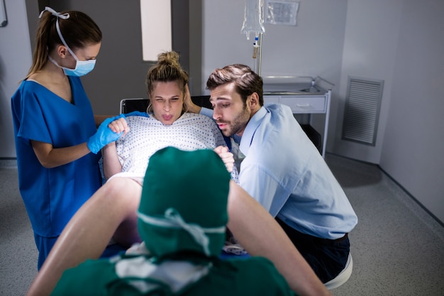 Bezpłatne zdjęcie doktorski egzamininuje kobieta w ciąży podczas dostawy podczas gdy mężczyzna trzyma jej rękę w sala operacyjnej