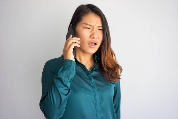Dokuczająca młoda Azjatycka kobieta w przypadkowej odzieży mówieniu na telefonie.