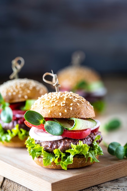 Domowe hamburgery z kotletem, świeżą sałatą, pomidorami, cebulą na drewnianym stole. skopiuj miejsce