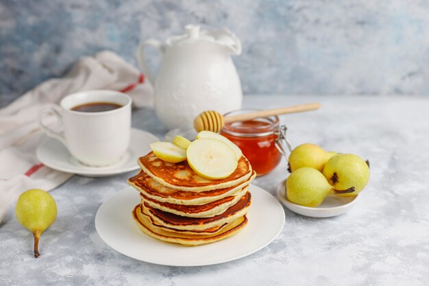 Domowe śniadanie: amerykańskie naleśniki podawane z gruszkami i miodem z filiżanką herbaty na betonie. Widok z góry i kopiowanie