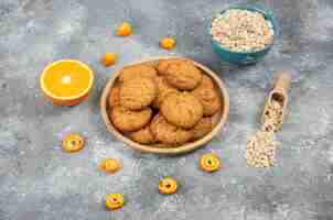 Bezpłatne zdjęcie domowe świeże ciasteczka na desce i płatki owsiane z pomarańczami na szarej powierzchni.