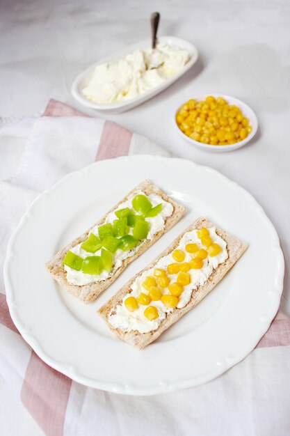 Domowy tost chrupiący z twarogiem i zielonymi oliwkami, plasterkami kapusty, pomidorów, kukurydzy, zielonego pieprzu na desce do krojenia. Koncepcja zdrowej żywności, widok z góry. Flat Lay