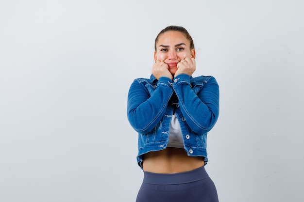 Dopasuj kobietę do poduszki twarzy na pięści w crop top, dżinsową kurtkę, legginsy i wyglądając wesoło. przedni widok.