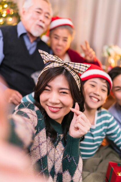 Dorosły Azjata daje pudełko prezentowe, aby zaprosić rodzica w święta Bożego Narodzenia podczas korzystania ze smartfona rozmawiając selfie zdjęcie szczęście razem w salonie na kanapierodzina relacja wiązanie wnętrze domu