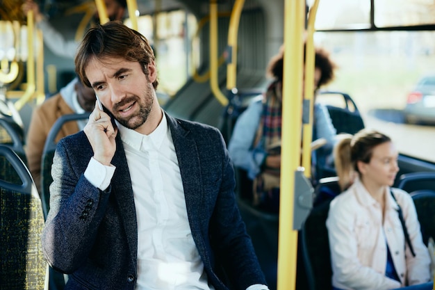 Dorosły biznesmen w średnim wieku rozmawia przez telefon podczas podróży autobusem do pracy