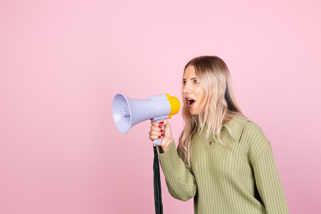 Dość europejska kobieta w swobodnym swetrze z megafonem na różowej ścianie