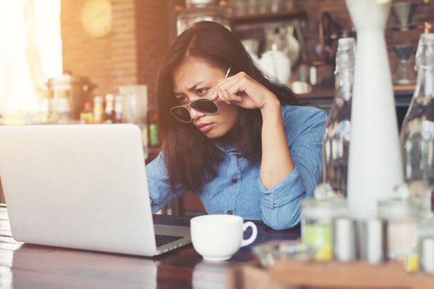 Dość młoda kobieta hipster siedzi w kawiarni z jej laptopa, lo