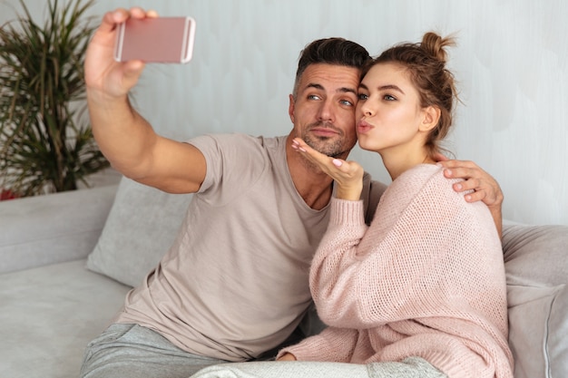 Dość urocza para siedzi na kanapie i robi selfie na smartphone w domu