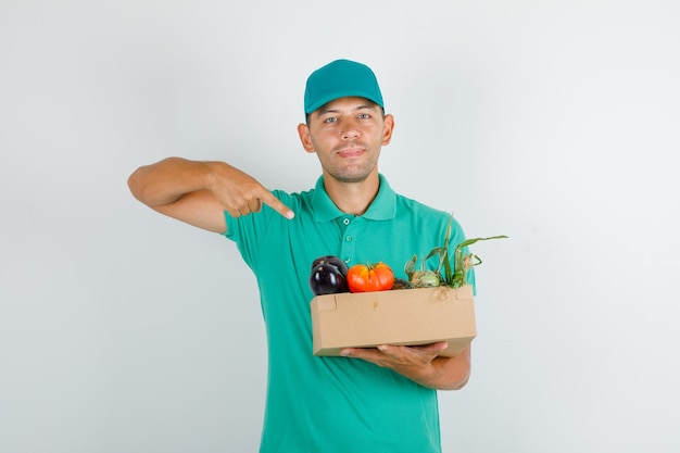 Dostawa Mężczyzna Wskazując Palcem Na Pudełko Warzyw W Zielonej Koszulce Z Czapką
