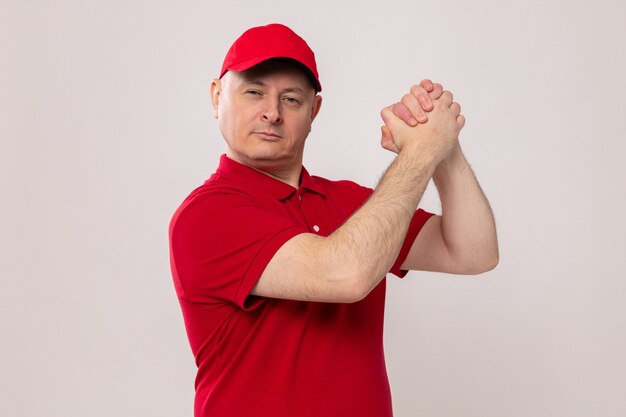 Dostawca w czerwonym mundurze i czapce, patrzący z pewnym siebie wyrazem, trzymający się za ręce, wykonujący gest pracy zespołowej
