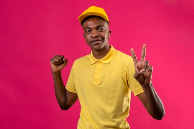 Dostawy Afroamerykanin w żółtej koszulce polo i czapce podnoszącej pięść pokazujący znak zwycięstwa palcami na różowo