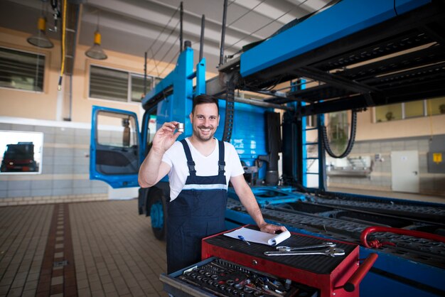 Doświadczeni mechanicy samochodów ciężarowych w średnim wieku trzymający części i narzędzia w warsztacie przy ciężarówce