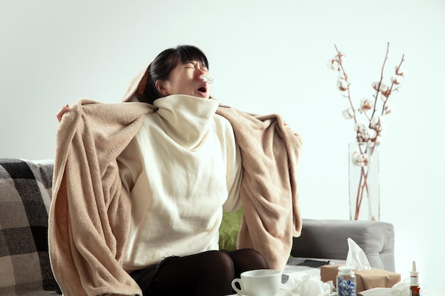Dreszcz. Młoda kobieta owinięta w kratę wygląda na chorą, chorą, kichając i kaszląc siedząc na kanapie w domu w domu.