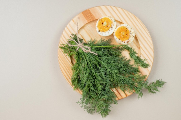 Bezpłatne zdjęcie drewniana deska z gotowanym jajkiem z przyprawami i zieleniną.