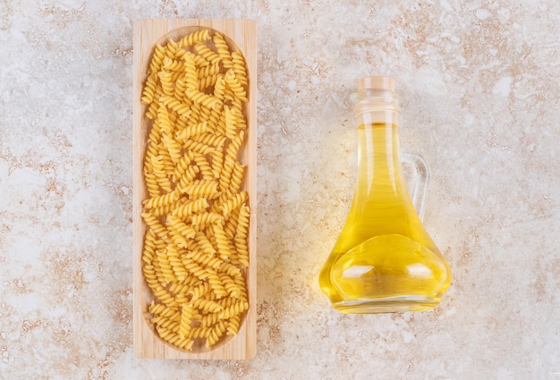 Bezpłatne zdjęcie drewniana deska z surowego spiralnego makaronu i szklana butelka oleju