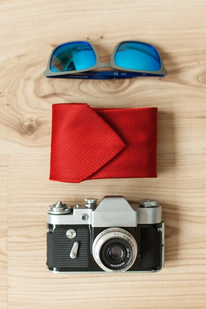 Drewniana powierzchnia z krawatem, okulary słoneczne i aparat fotograficzny