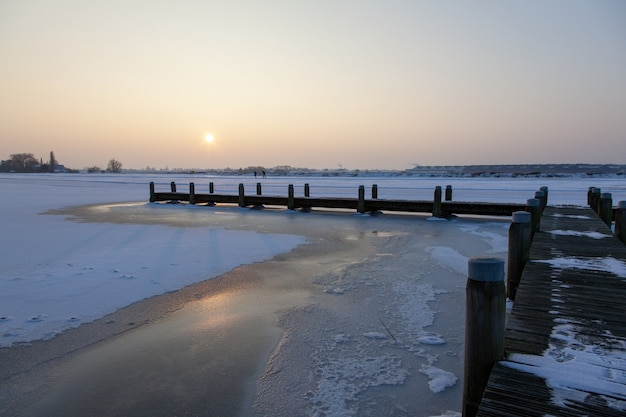 Drewniana ścieżka nad zamarzniętą wodą z zamglonym niebem