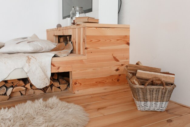 Drewniane łóżko i drewno opałowe pod nim, kosz pełen kominka