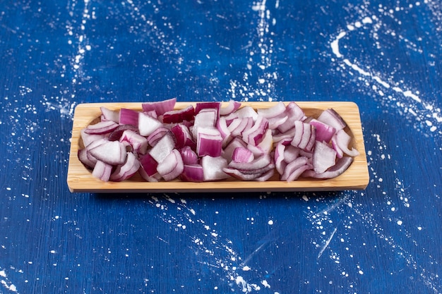 Bezpłatne zdjęcie drewniany talerz pokrojonej w plasterki fioletowej cebuli na marmurowym stole.