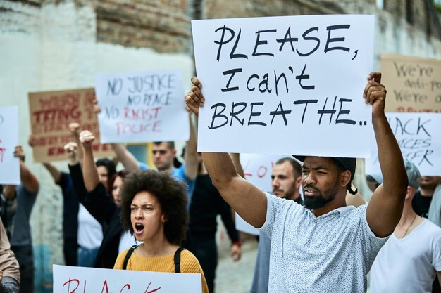 Duża grupa ludzi na proteście Black Lives Matter Koncentruje się na czarnym mężczyźnie trzymającym tabliczkę z napisem „Proszę, nie mogę oddychać”