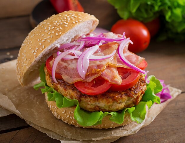 Duża kanapka - burger hamburgerowy z wołowiną, czerwoną cebulą, pomidorem i smażonym boczkiem.