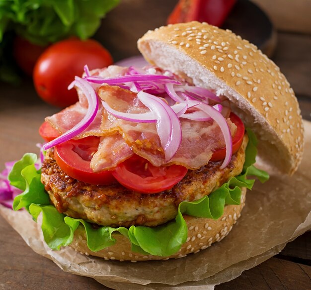 Duża kanapka - burger hamburgerowy z wołowiną, czerwoną cebulą, pomidorem i smażonym boczkiem.