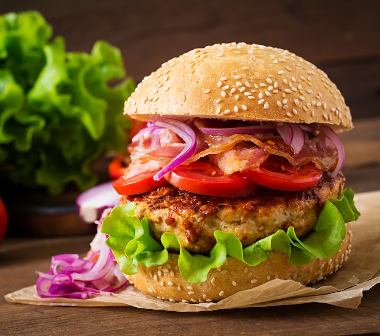 Bezpłatny plik Zdjęcie duża kanapka - burger hamburgerowy z wołowiną, czerwoną cebulą, pomidorem i smażonym boczkiem.