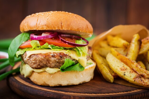 Duża kanapka - hamburger z soczystym burgerem wołowym, serem, pomidorem i czerwoną cebulą na drewnianym stole