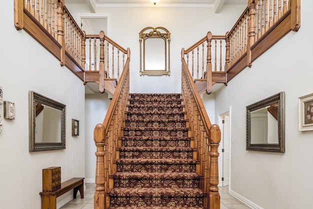 Duże drewniane schody z zabytkowym dywanem wewnątrz mieszkania o białych ścianach