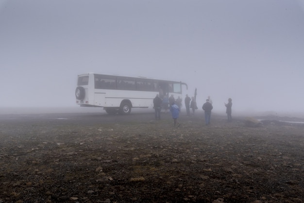 Duży biały autobus i grupa ludzi w jego pobliżu przy mglistej pogodzie na Islandii