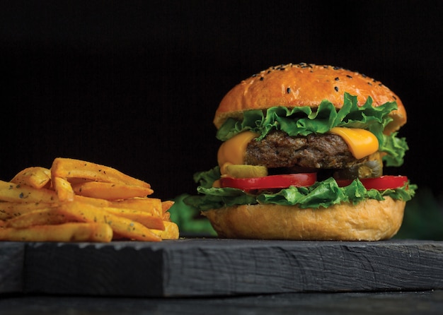 Duży Mac burger i frytki na desce z ciemnego drewna.