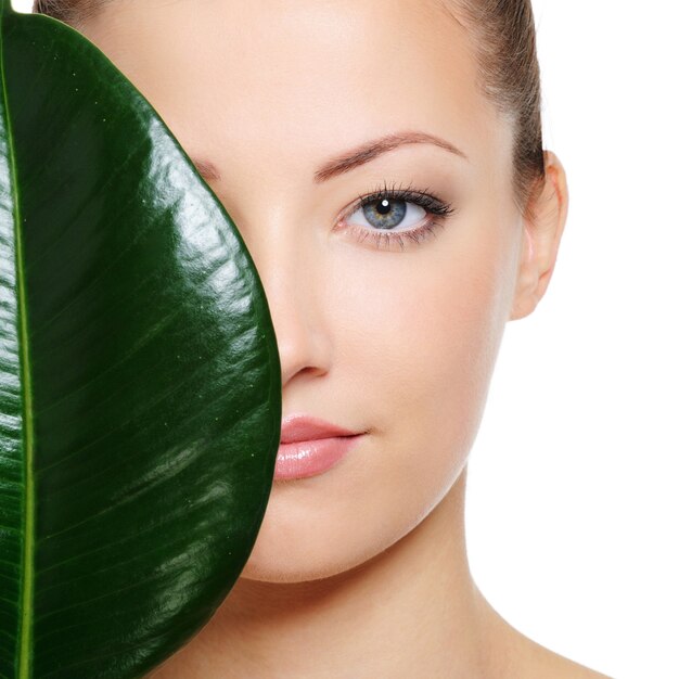 Duży zielony liść cieniujący połowę pięknej twarzy kobiety na białej przestrzeni