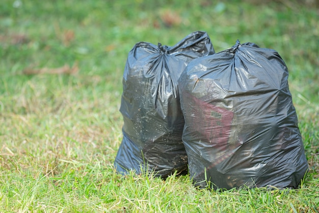 Dwa czarne worki na śmieci postawione na podłodze z trawy