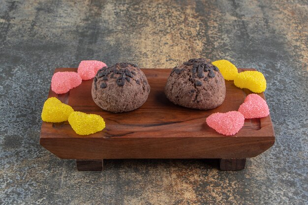Dwa czekoladowe ciasteczka i cukierki marmoladowe na drewnianym talerzu