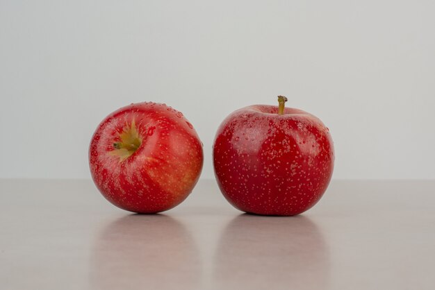 Dwa czerwone jabłka na marmurowym stole.