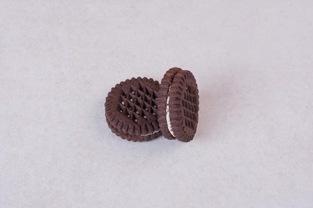 Dwa, małe, słodkie ciasteczka czekoladowe na białym stole.