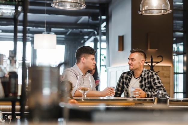 Bezpłatne zdjęcie dwa męskiego przyjaciela siedzi przy baru kontuaru mieniem piją