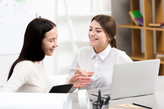 Dwa młody bizneswoman śmia się podczas gdy dyskutujący projekt na laptopie