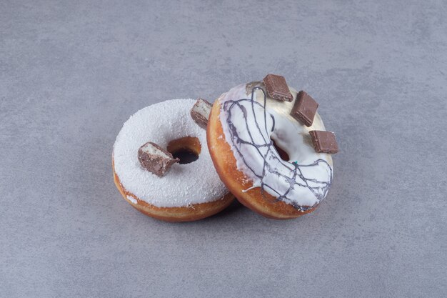 Dwa pączki ozdobione czekoladą na marmurowej powierzchni