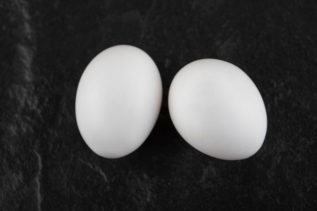 Dwa świeże białe jaja kurze na czarnym stole.